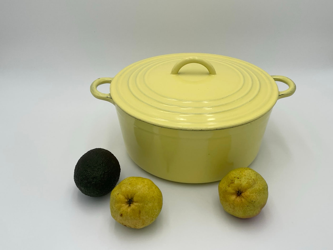 Vintage Le Creuset round cocotte in pale yellow enamel with an arched cast lid handle and loop side handles