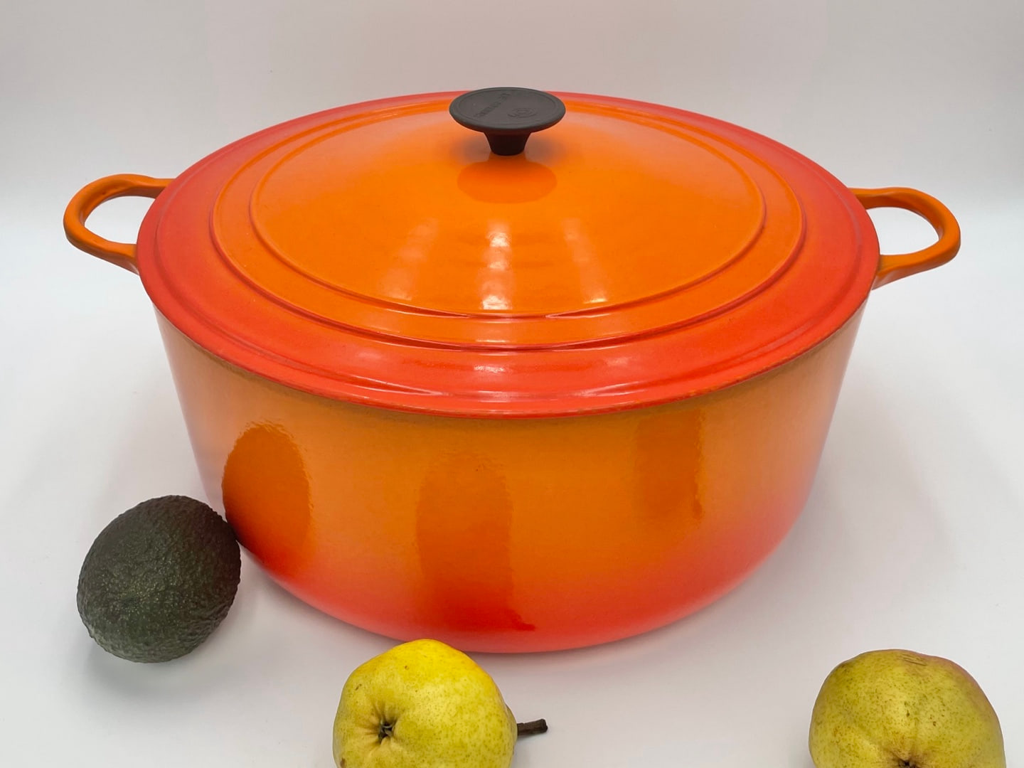 Vintage Le Creuset round cocotte in orange enamel with a black disc lid knob and loop side handles