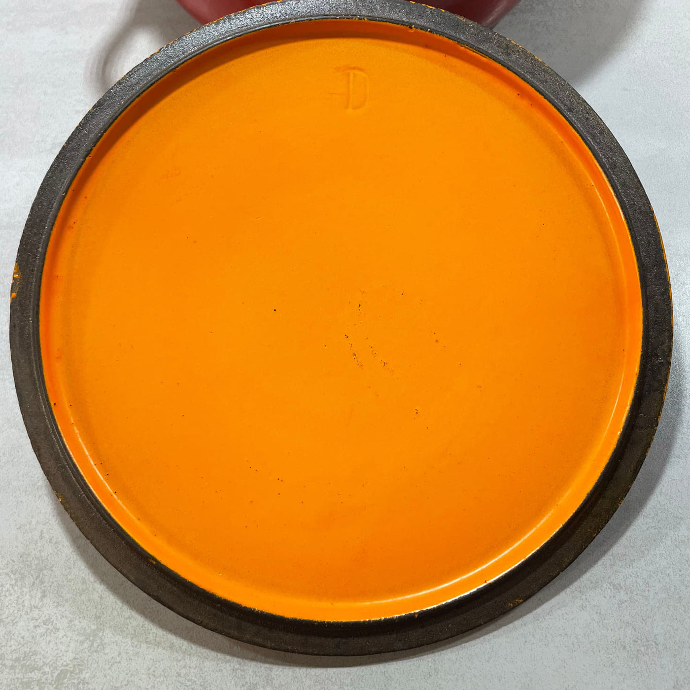 Underside of an early Le Creuset cocotte lid showing rim construction, enamel and a casting mark